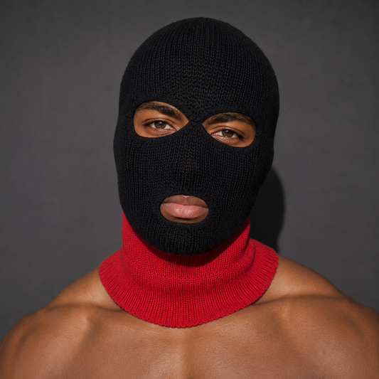 A man wearing a black knit balaclava mask with a red knit neck gaiter, shown from the chest up against a dark gray background.