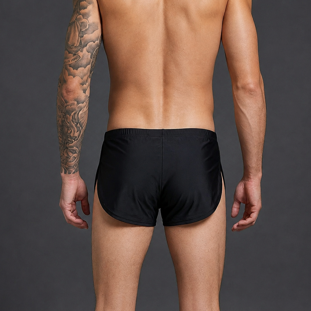 Rear view of a shirtless man wearing black swim trunks against a dark gray studio background.